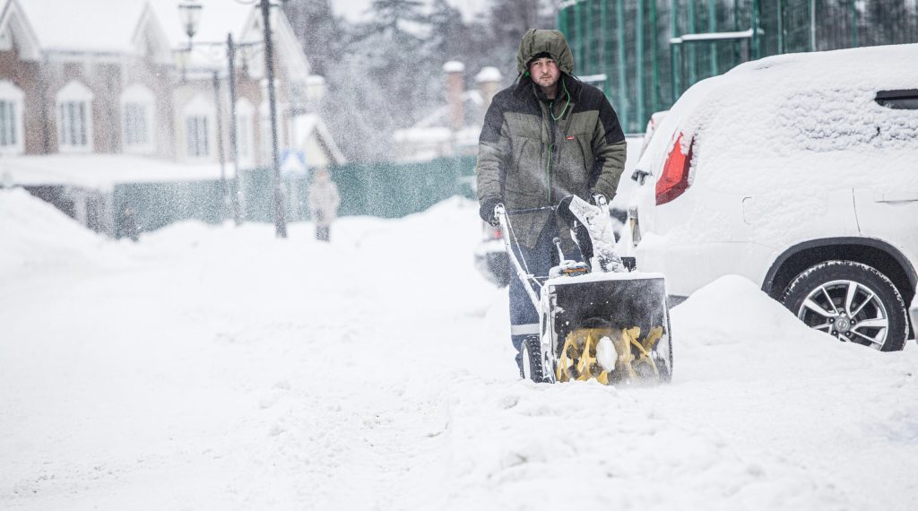 A man using a snow blower to clear snow from a snowy street during winter.