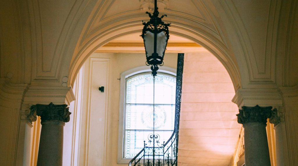 Majestic interior featuring a classic staircase with ornate columns and a large window for natural light.